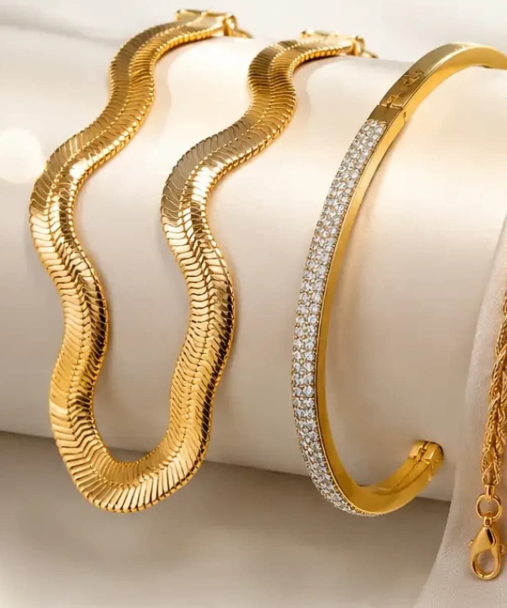 Duas correntes de malha lisa e uma bracelete cravejada, banhadas a ouro 18k, sobre seda creme